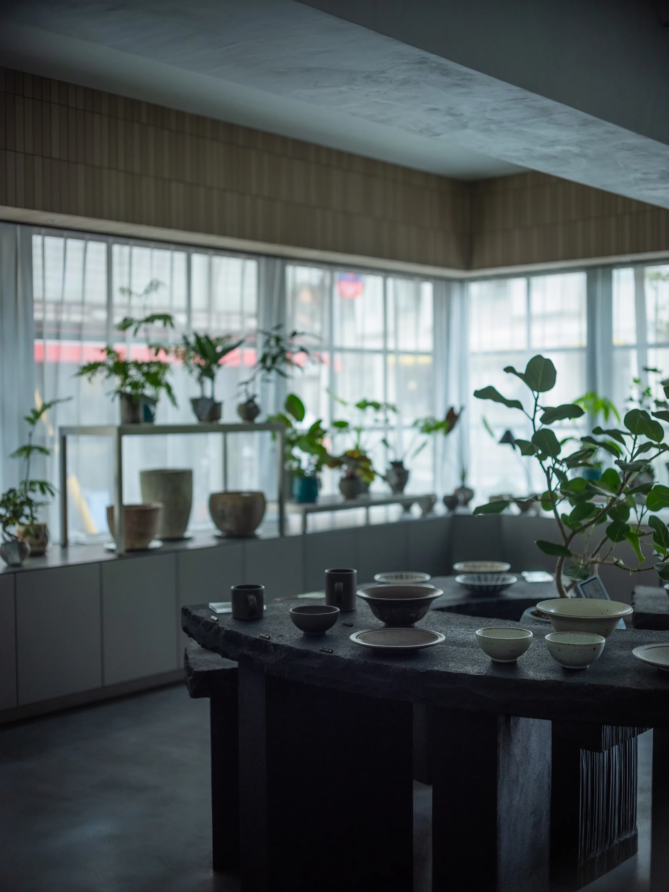 窓辺の植木鉢と黒いテーブルに置かれた器、柔らかな光の空間